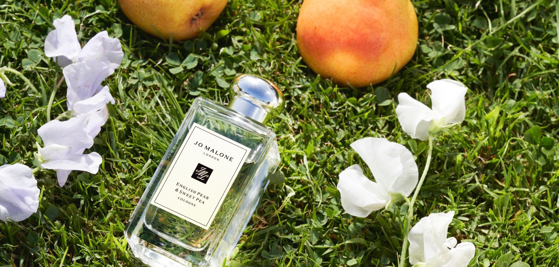 Jo Malone London English Pear & Sweet Pea Colognes lying on grass surrounded by pears and white flowers