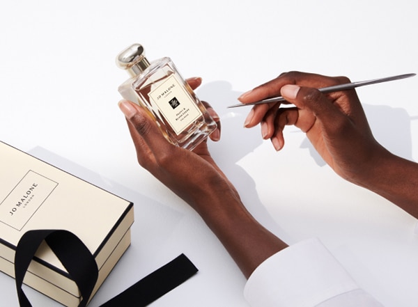 Jo Malone London Cologne Bottle being held in hand with engraving tool and cream box in the background